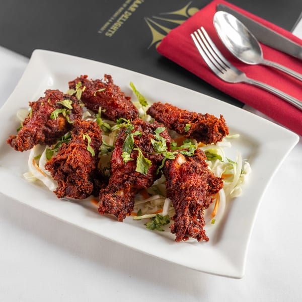 Pariwaar Delights' Chicken 65, crispy red fried chicken pieces on a bed of shredded cabbage.