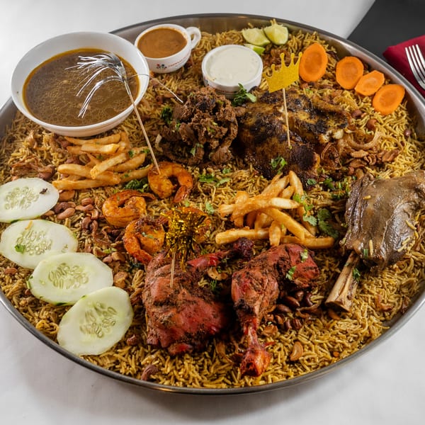 A large platter of Indian biryani with chicken, lamb, shrimp, fries, and sauces.