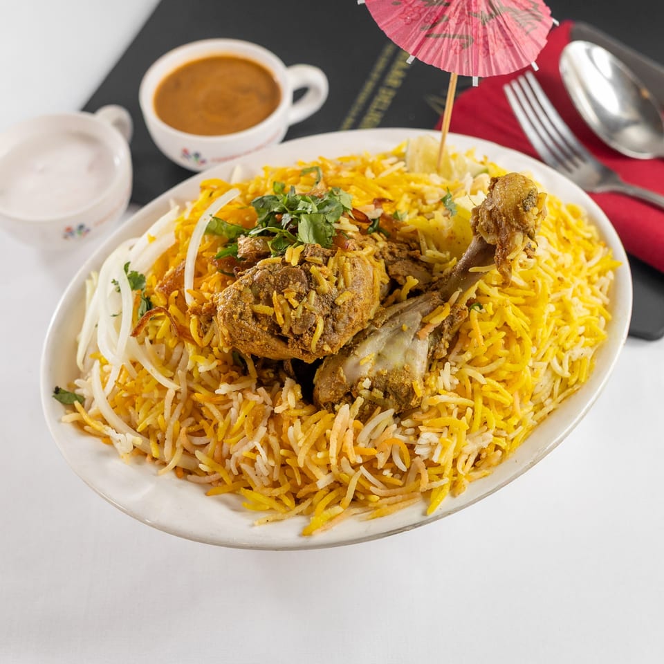 A plate of Pariwaar Delights' chicken biryani with rice, onions, cilantro, and a side of sauce.