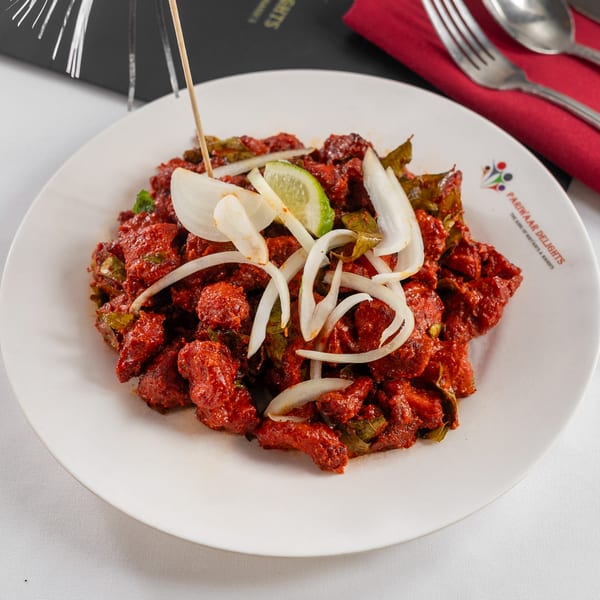 Pariwaar Delights' red Indian chicken dish, garnished with onions and lime, on a white plate.