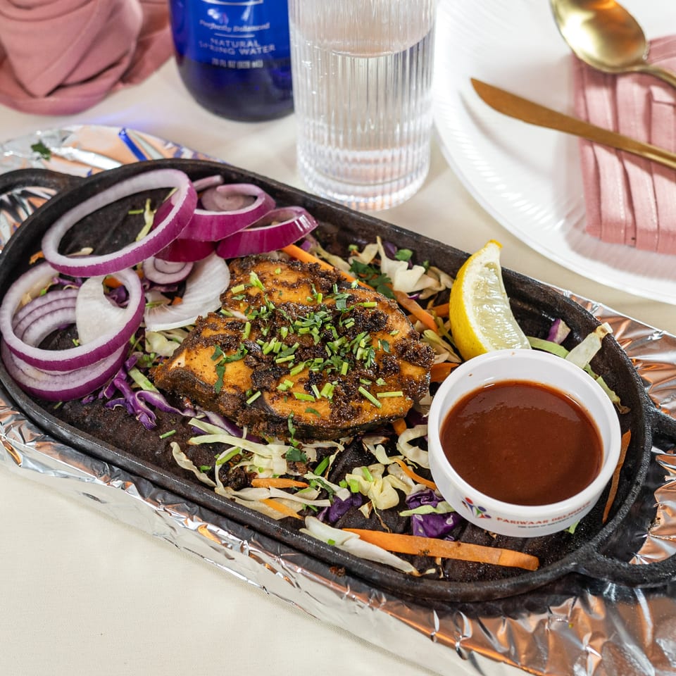 Indian fish fry with red onions, cabbage, lemon, and sauce on a hot plate.