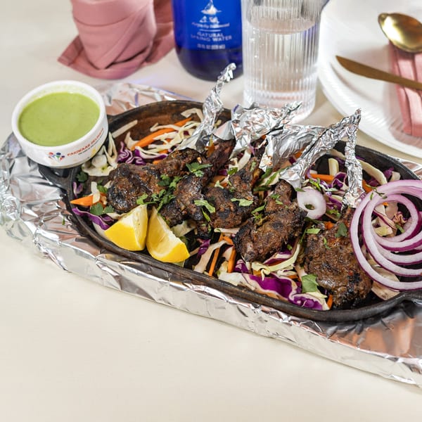 Pariwaar Delights' sizzling lamb chops with foil-wrapped bones, lemon, and a side of green chutney.