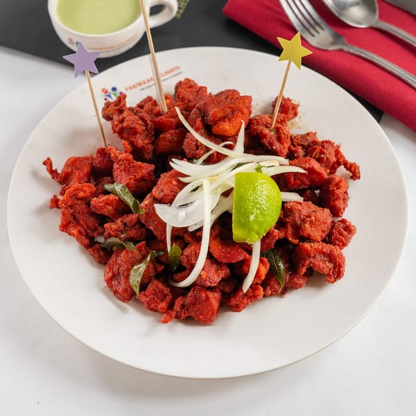 Pariwaar Delights' Chicken 65, a vibrant red Indian dish, garnished with onions and lime.