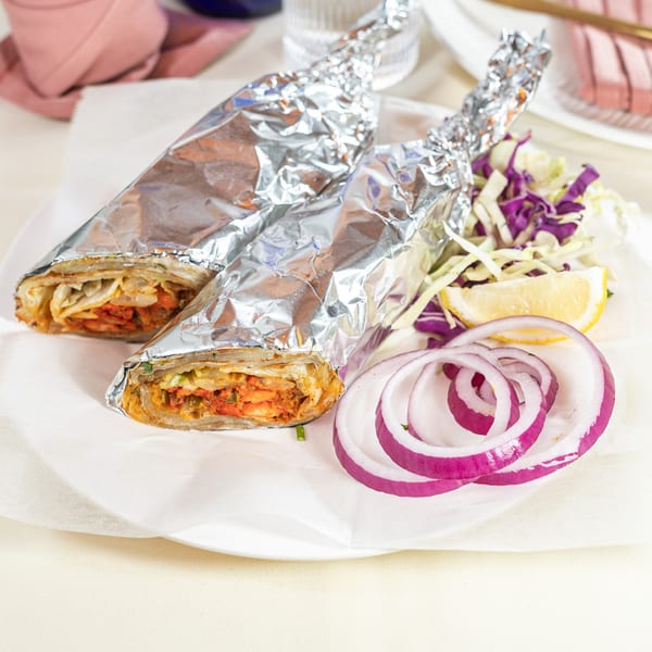 Two Indian kathi rolls wrapped in foil, served with red onion, cabbage, and a lemon wedge.