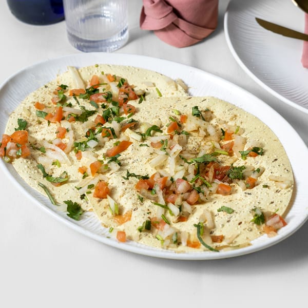 Pariwaar Delights' papadum topped with diced tomatoes, onions, and fresh cilantro on a white platter.