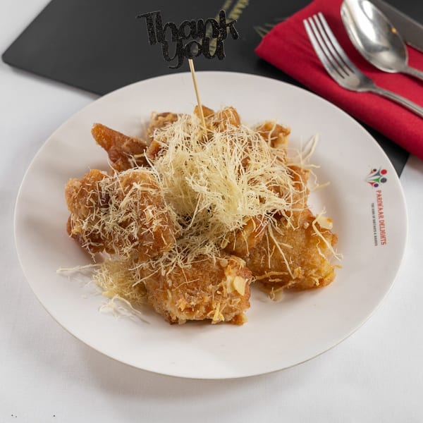 Golden fried dessert pieces topped with shredded cheese and a "Thank You" pick on a white plate.