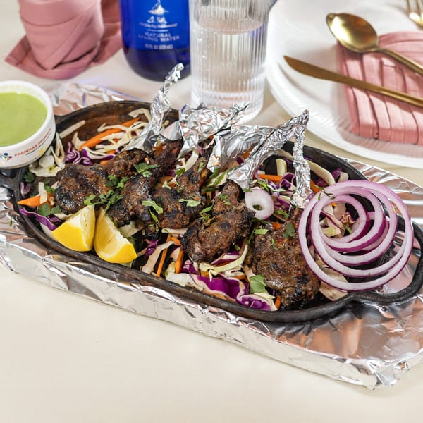 Indian lamb chops with foil-wrapped bones, lemon, red onion, and cabbage on a sizzling platter.