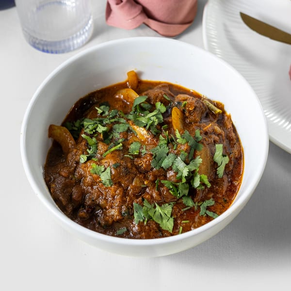 A white bowl filled with rich, dark Indian curry, garnished with fresh green cilantro.