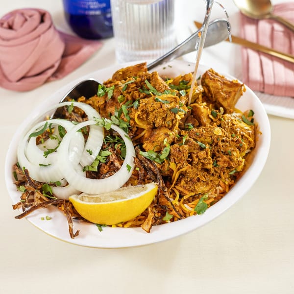 Pariwaar Delights' chicken biryani with onions, fried shallots, cilantro, and a lemon wedge.