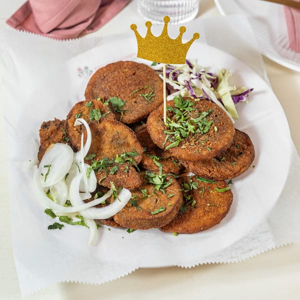 Pariwaar Delights' Indian dish with fried patties, onions, cilantro, and a golden crown pick.