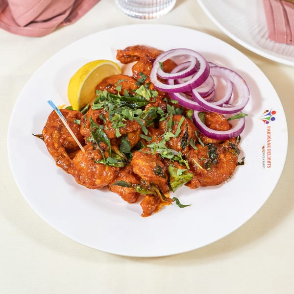 Pariwaar Delights' Indian chicken dish, garnished with red onions, cilantro, and a lemon wedge.