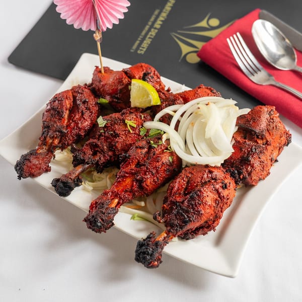 Pariwaar Delights' Tandoori chicken drumsticks with onions and lime, served on a white plate.