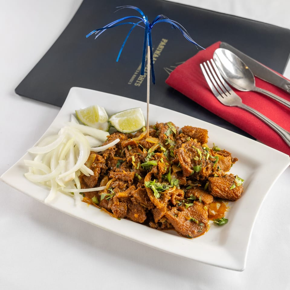 Pariwaar Delights' Indian dish with meat, onions, lime, and cilantro, served on a white plate.
