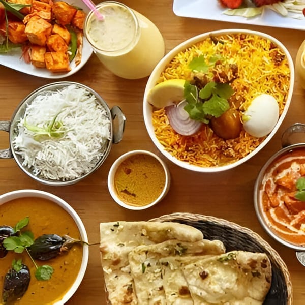 A variety of Indian dishes including biryani, curries, naan, and a mango lassi on a wooden table.