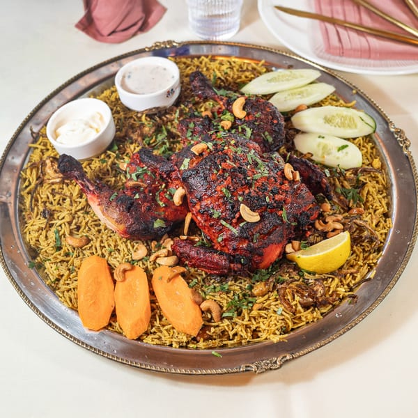 Pariwaar Delights' chicken biryani with red chicken, cashews, lemon, cucumber, and sauces on a silver platter.