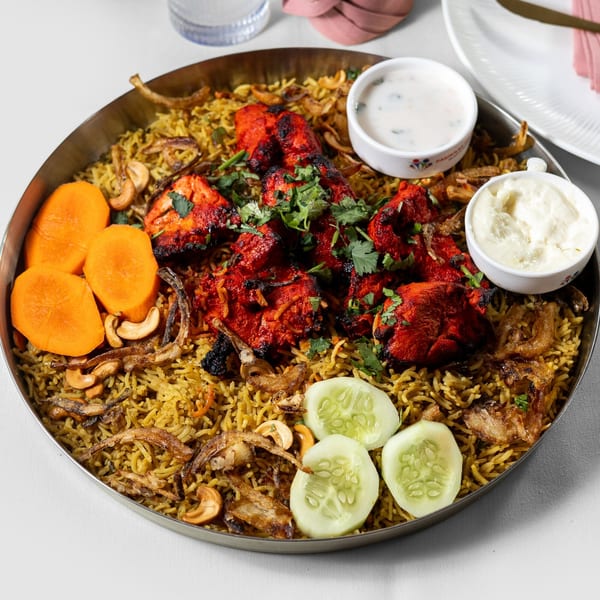 Pariwaar Delights' chicken biryani with red chicken pieces, cashews, carrots, cucumbers, and sauces.
