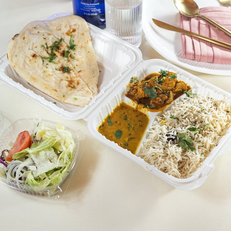 Indian takeout meal with naan, rice, curry, dal, and a side salad on a light tablecloth.