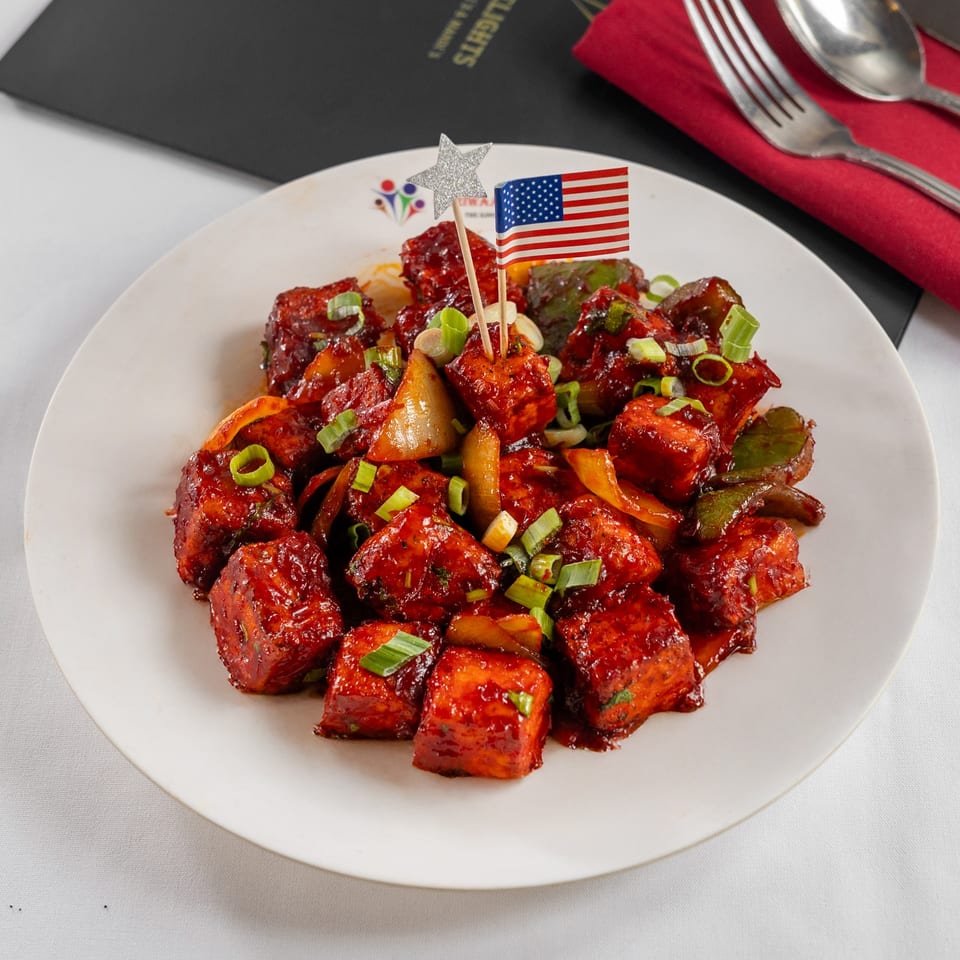 Pariwaar Delights' chili paneer, garnished with green onions and an American flag pick.