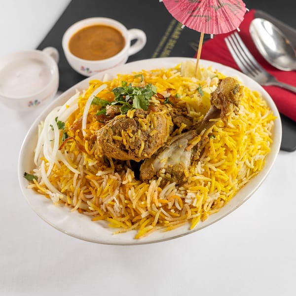 A plate of chicken biryani with rice, onions, and cilantro, served with two dipping sauces.