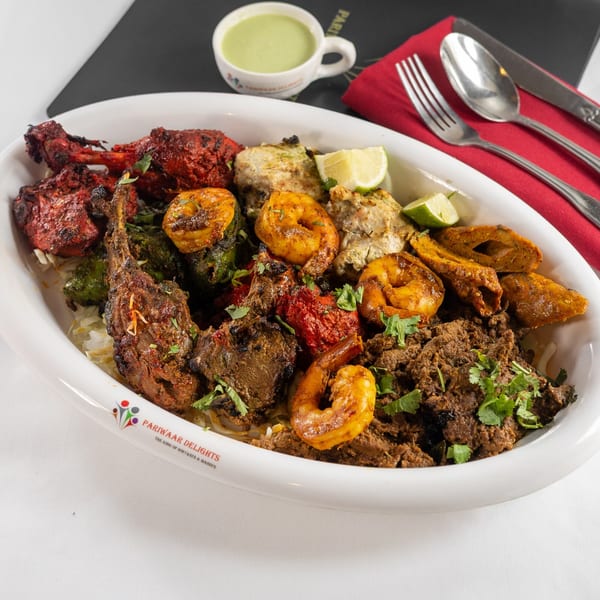 A large platter of various Indian grilled meats, including chicken, lamb, and shrimp, with lime wedges.