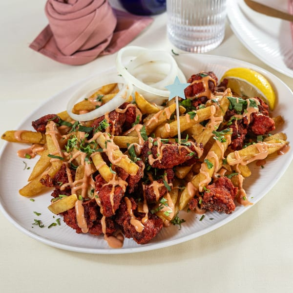 Pariwaar Delights' Chicken 65 with fries, sauce, onions, and a lemon wedge on a white plate.