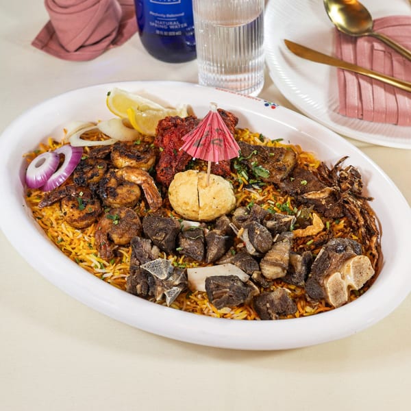 A large platter of Indian biryani with shrimp, mutton, chicken tikka, and a boiled egg.