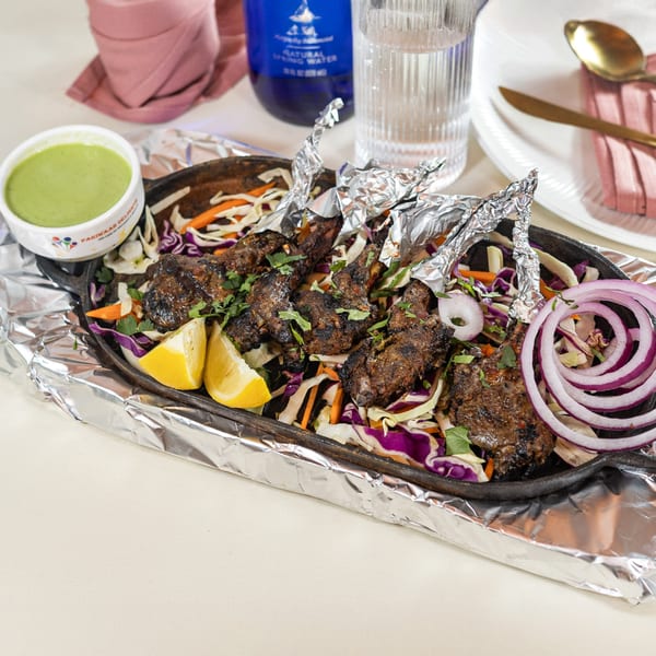 Pariwaar Delights' grilled lamb chops with foil-wrapped bones, served on a bed of colorful slaw with lemon and sauce.
