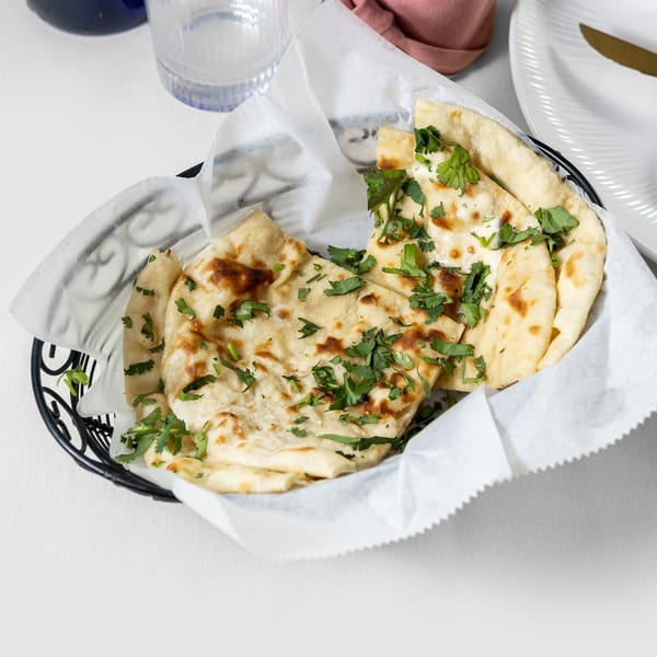 A black basket filled with warm, golden-brown naan bread, garnished with fresh green cilantro.