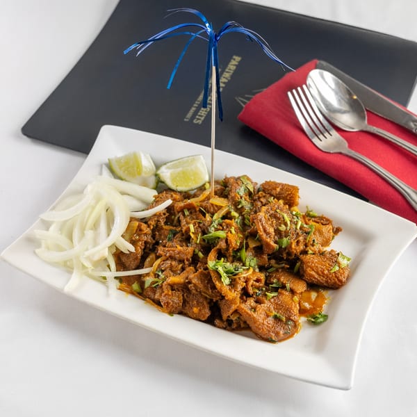 Pariwaar Delights' Indian dish with meat, onions, lime, and cilantro, served on a white plate.