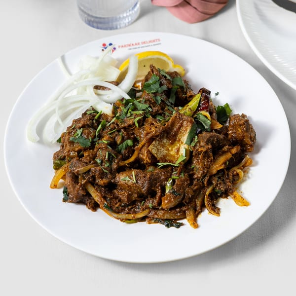 Pariwaar Delights' Indian lamb or goat curry with onions, cilantro, and lemon on a white plate.