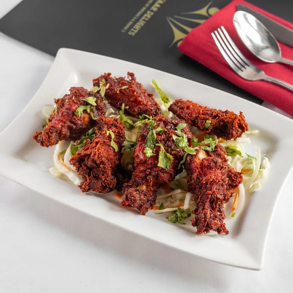 Pariwaar Delights' Chicken 65, crispy red fried chicken drumettes on a bed of shredded cabbage.