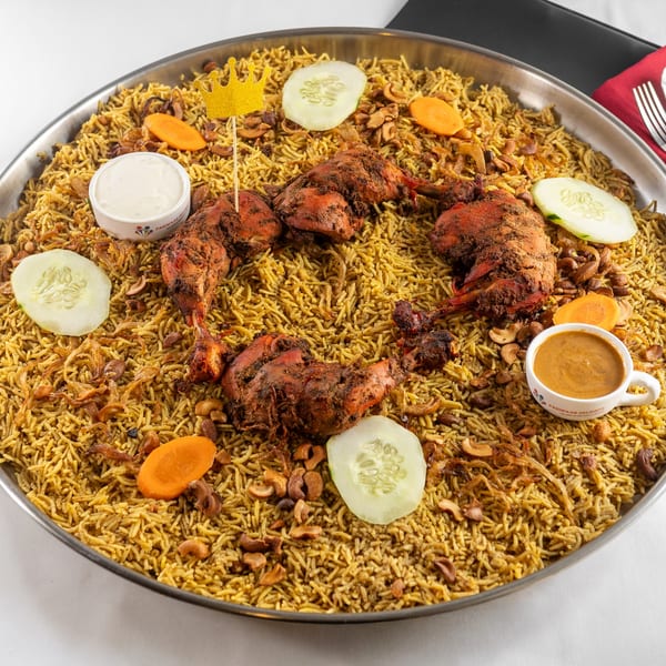 Pariwaar Delights' chicken biryani with roasted chicken, cashews, fried onions, and sauces in a large platter.