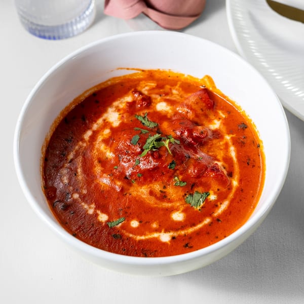 A white bowl of vibrant red Indian butter chicken, garnished with cream swirls and fresh cilantro.