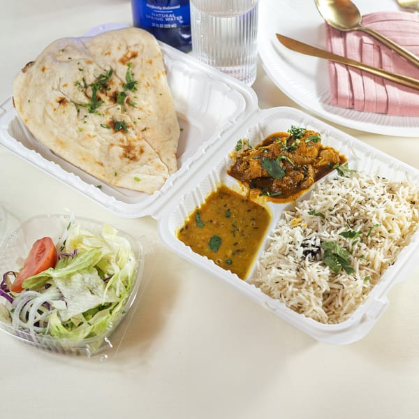 Indian takeout meal with naan, rice, curry, dal, and a side salad on a light tablecloth.