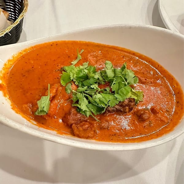 A white oval dish filled with vibrant orange Indian curry, garnished with fresh green cilantro.