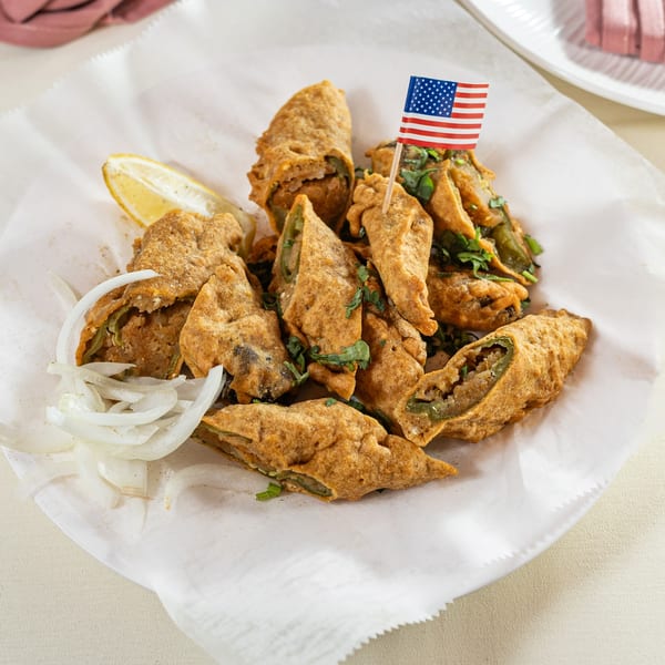 Fried green chili fritters, garnished with cilantro, sliced onions, and a lemon wedge, with an American flag pick.