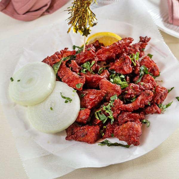 Pariwaar Delights' red chicken 65, garnished with cilantro, curry leaves, onions, and lemon.