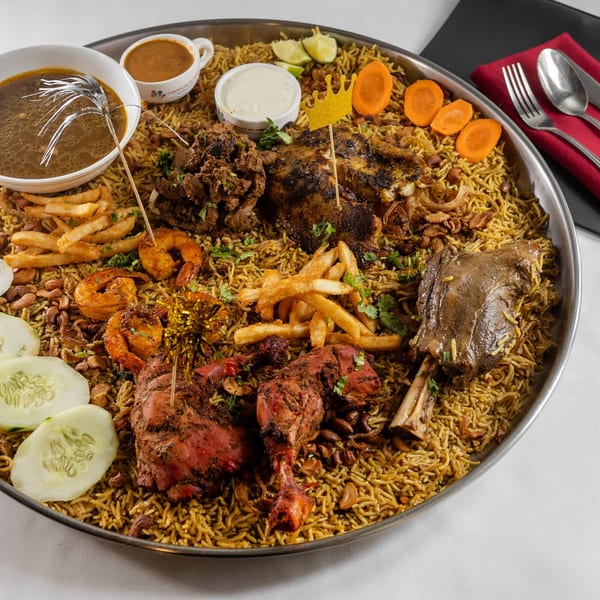 A large platter of Pariwaar Delights' biryani with various meats, shrimp, fries, and sauces.