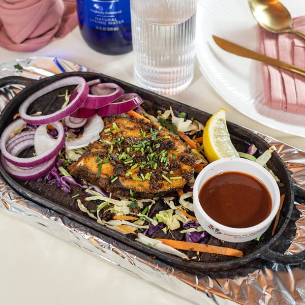Indian fish fry with red onions, cabbage, lemon, and sauce on a hot plate.