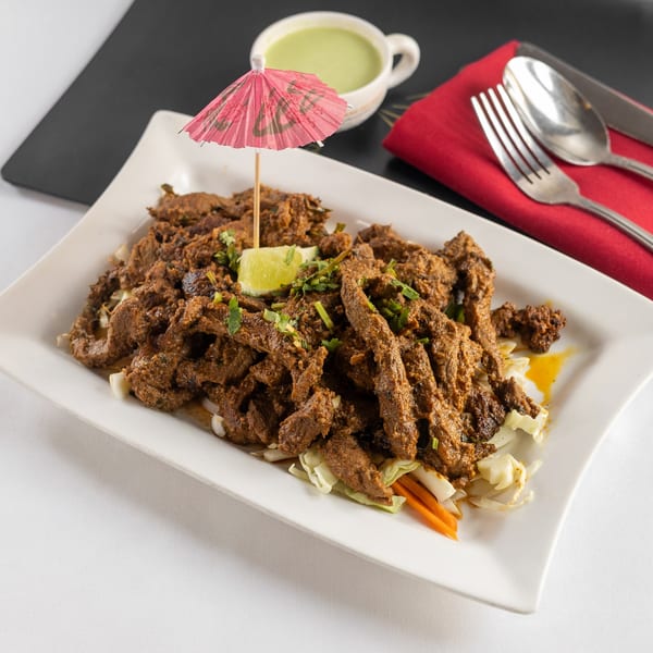Indian-style beef fry, garnished with lime and cilantro, served with a green dipping sauce.
