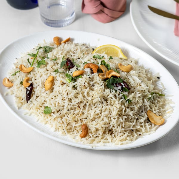 Pariwaar Delights' Indian biryani with cashews, cilantro, and a lemon wedge on a white platter.