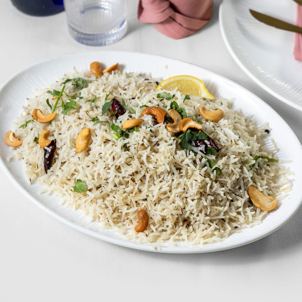 Pariwaar Delights' Indian biryani with cashews, cilantro, and a lemon wedge on a white platter.