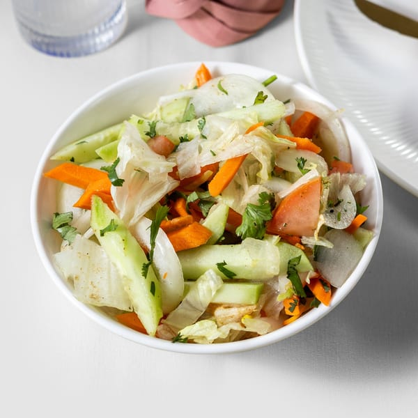 A white bowl filled with a fresh Indian salad of lettuce, carrots, cucumbers, and onions.