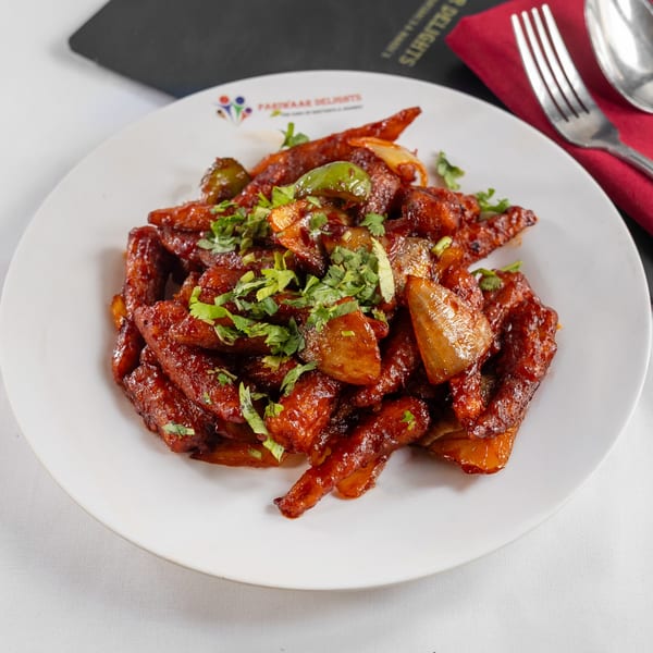 Chilli Paneer, an Indian appetizer, with green peppers, onions, and cilantro on a white plate.