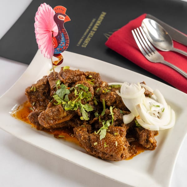 Pariwaar Delights' Indian curry dish with meat, cilantro, and onions, served on a white plate.