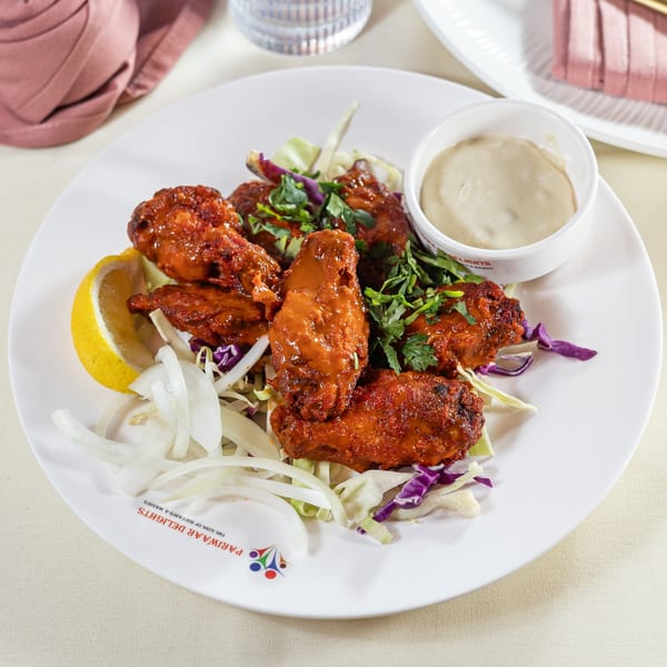 Pariwaar Delights' chicken wings, garnished with cilantro, onions, lemon, and a side of dipping sauce.