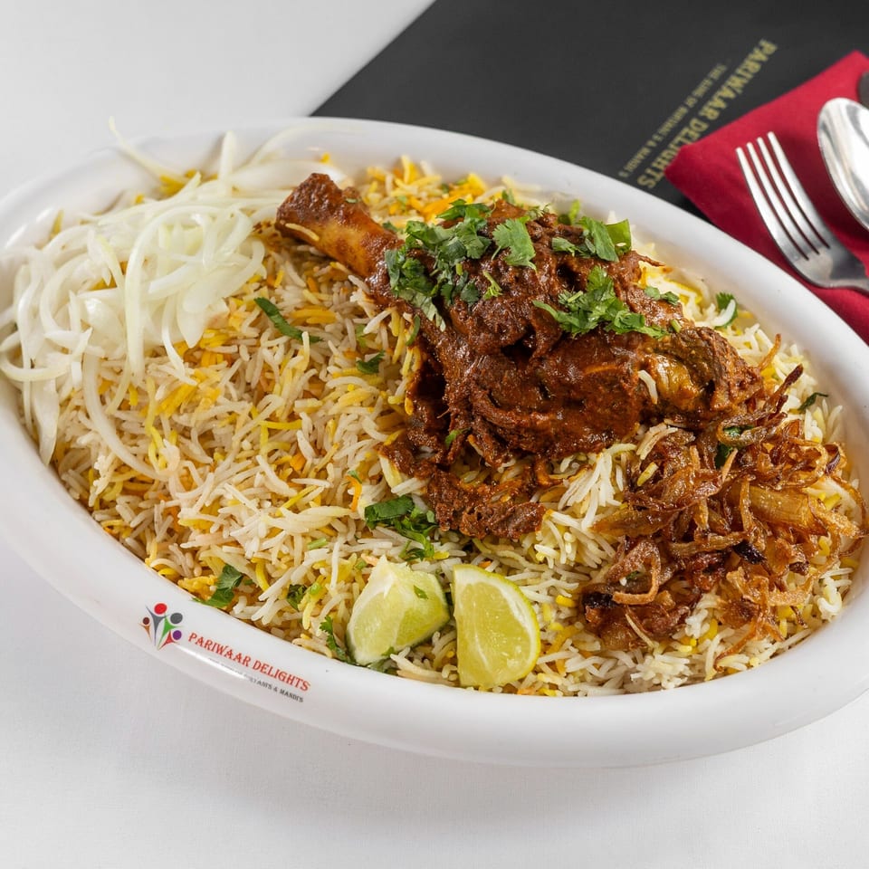 Pariwaar Delights' lamb biryani with rice, meat, fried onions, cilantro, and lime wedges.