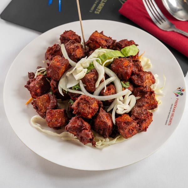 Pariwaar Delights' Chicken 65, a vibrant red Indian fried chicken dish, garnished with onions and lettuce.