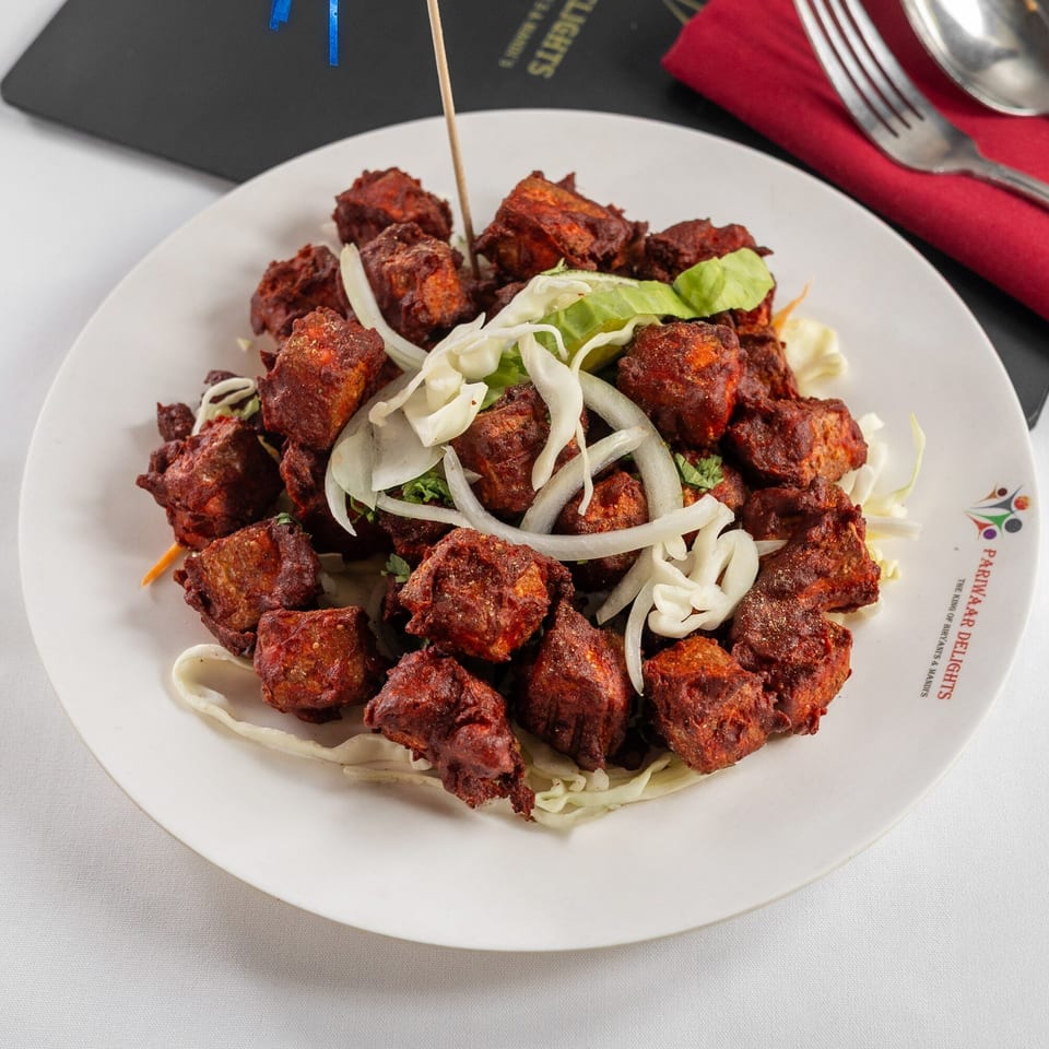 Pariwaar Delights' Chicken 65, a vibrant red Indian fried chicken dish, garnished with onions and lettuce.