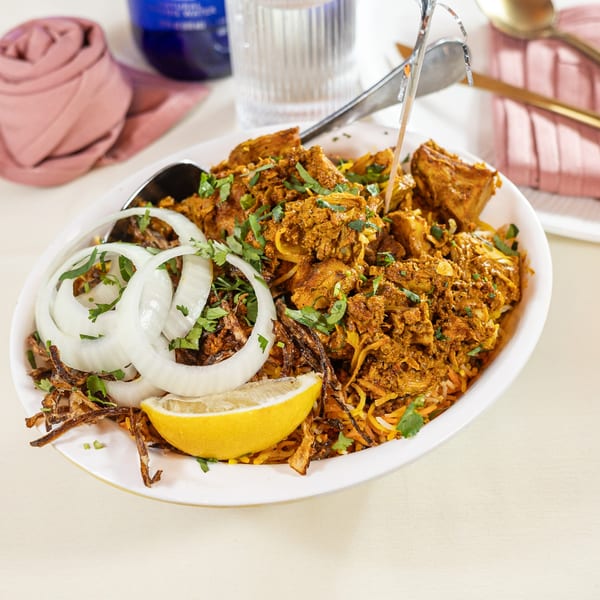 Pariwaar Delights' chicken biryani with sliced onions, fried onions, lemon, and cilantro in a white dish.